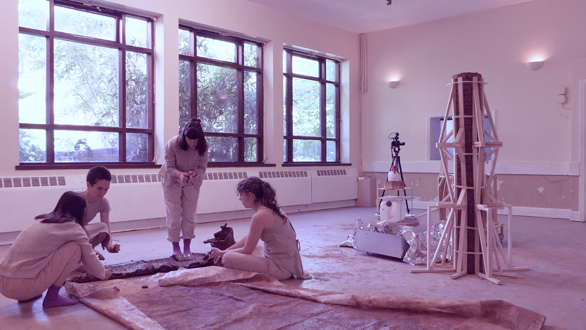 An image of several people building a column in a pink-tinted room.