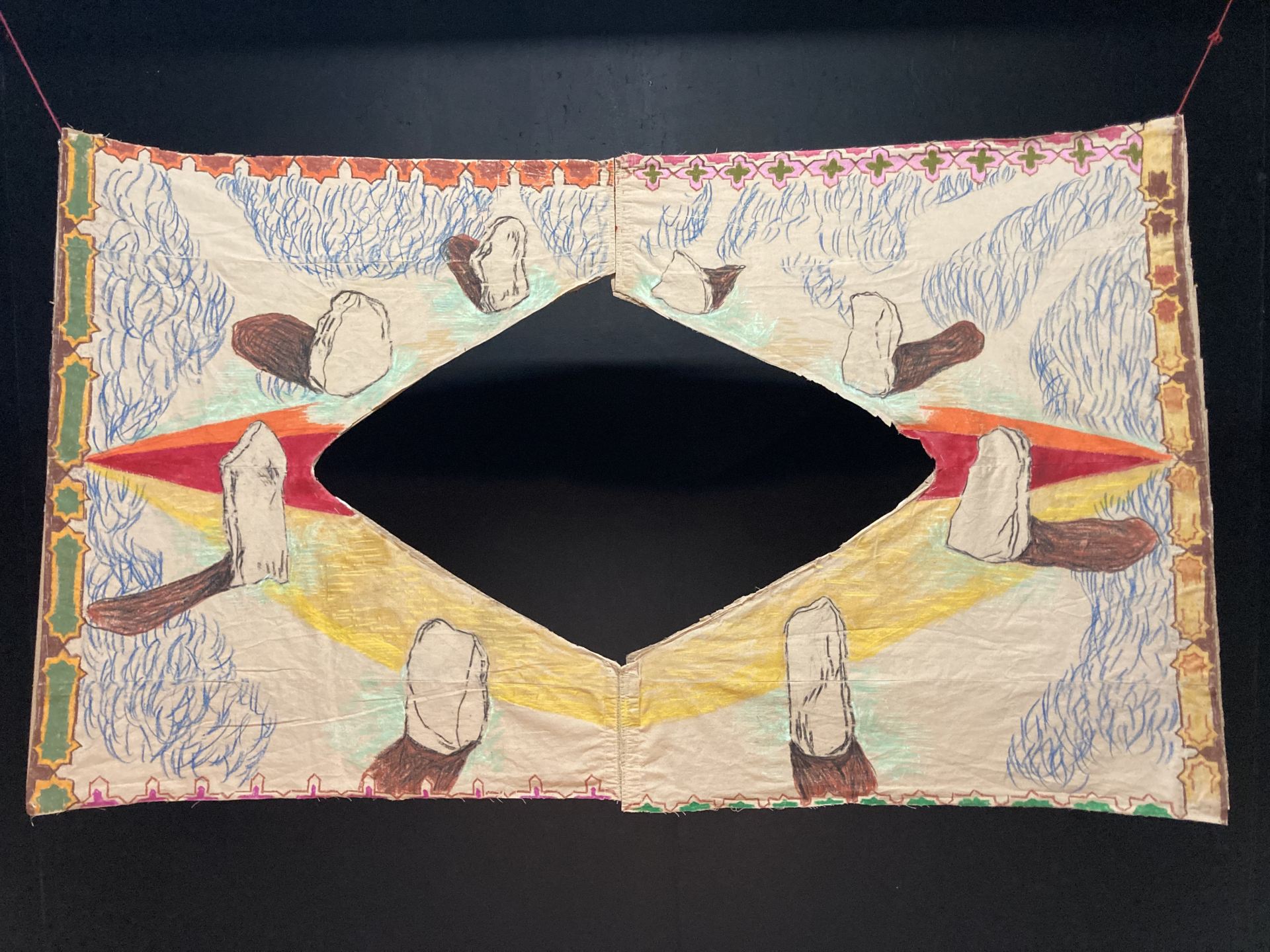 An oil pastel drawing of a stone circle with shadows on a pair of shalwar (trousers), stitched onto cardboard with decorative motifs around border.