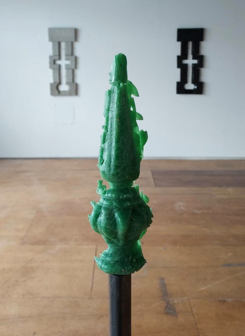 A railing finial cast made with green alcohol bottle glass on top of a steel post flanked either side with medieval arrow holes made from ceramics.