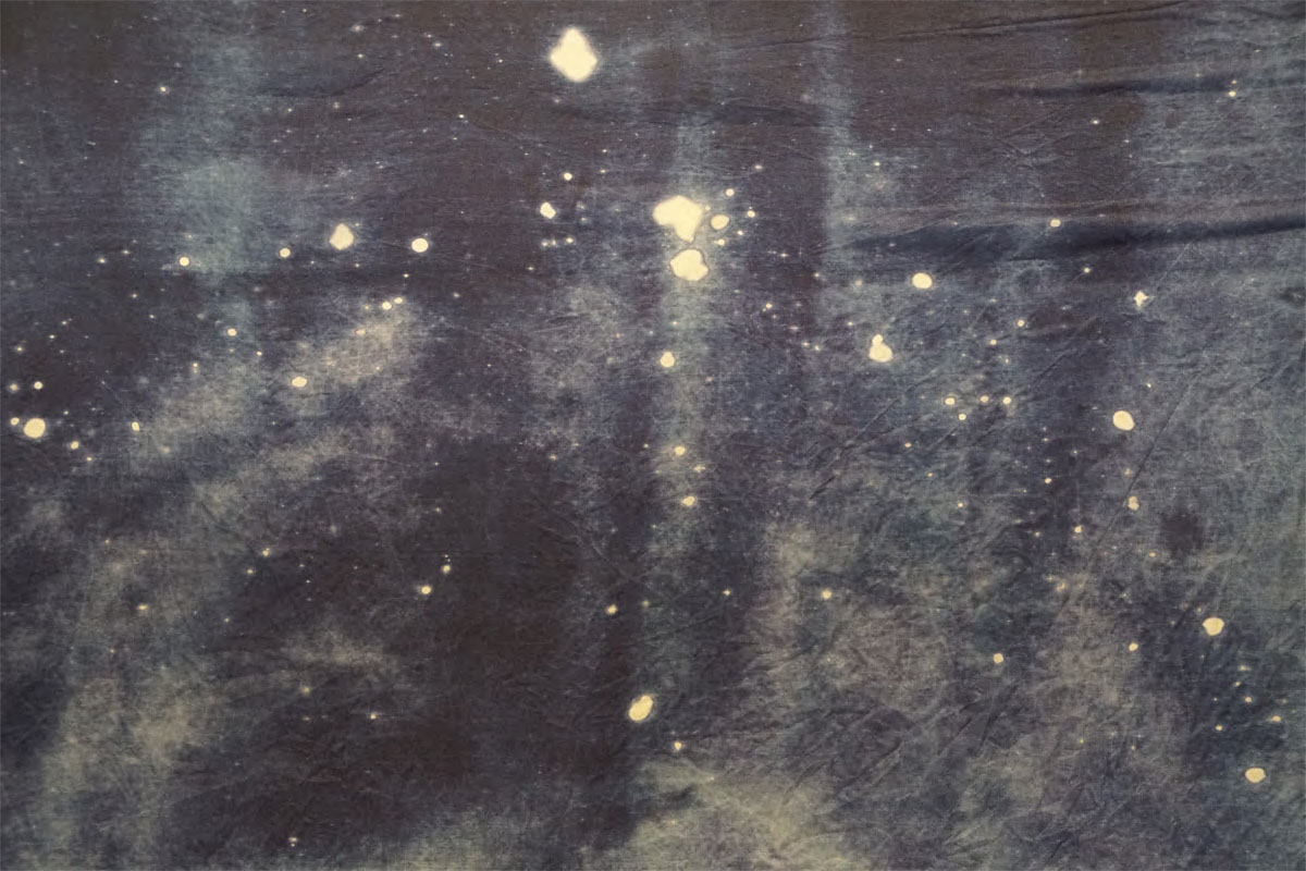 An image of a galaxy-like photogram on silk. There are bright white specs of various sizes against a deep blue background.
