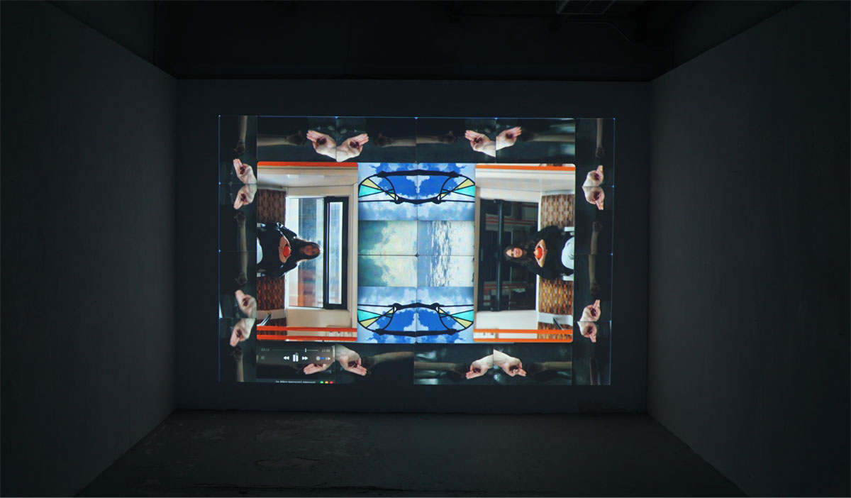 A video still from a projection in a dark room. The projection is an almost symmetrical, kaleidoscopic, composition of iPhone film clips.