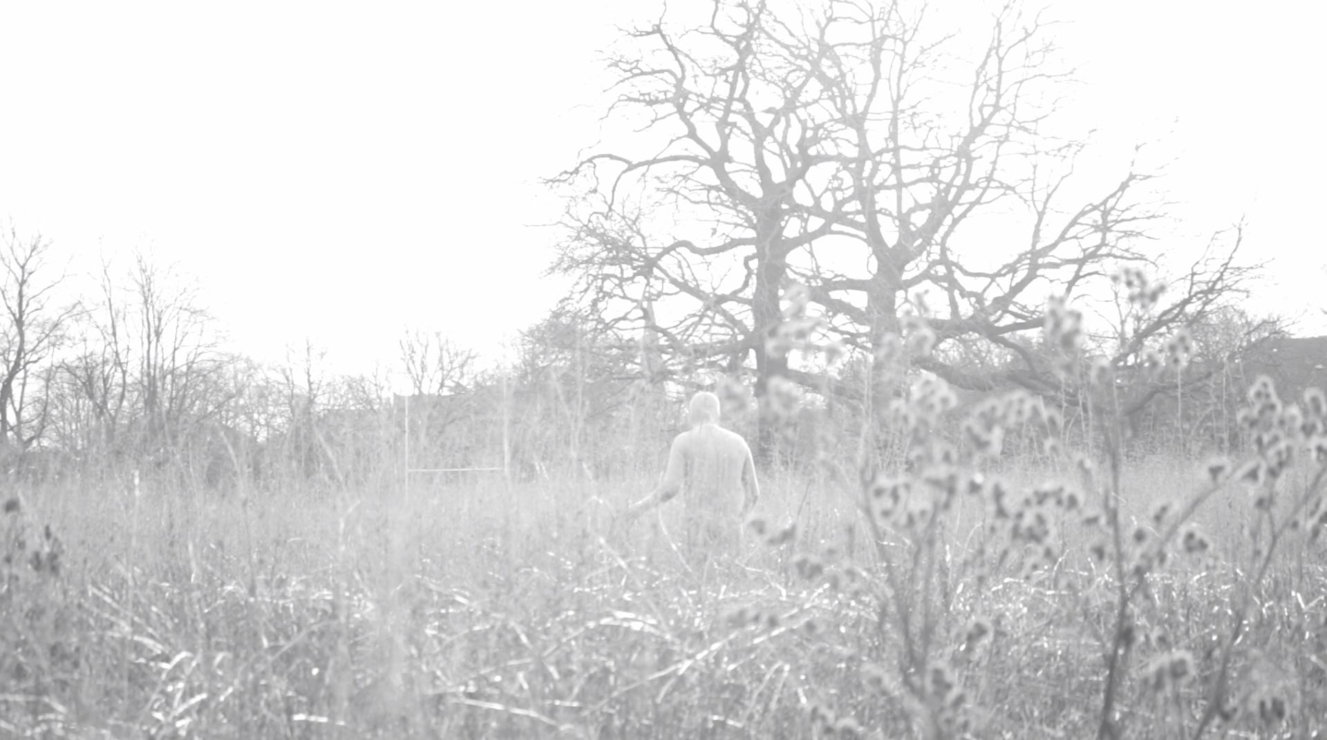 A greyscale video still of a person standing in a field.