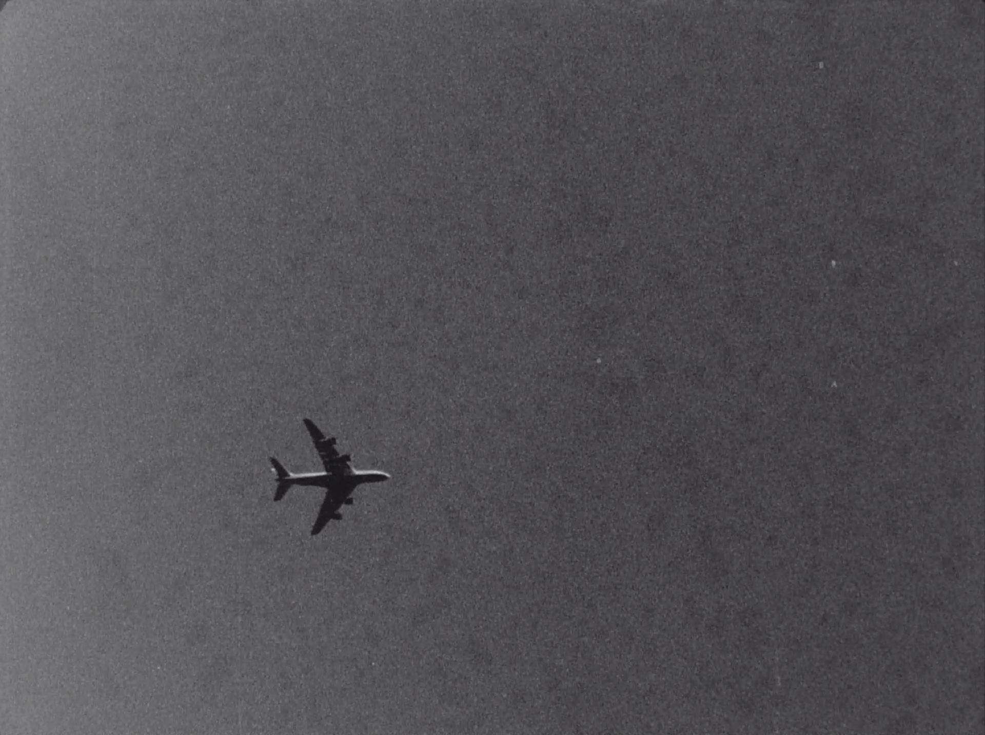 A greyscale video still of a plane in the sky.