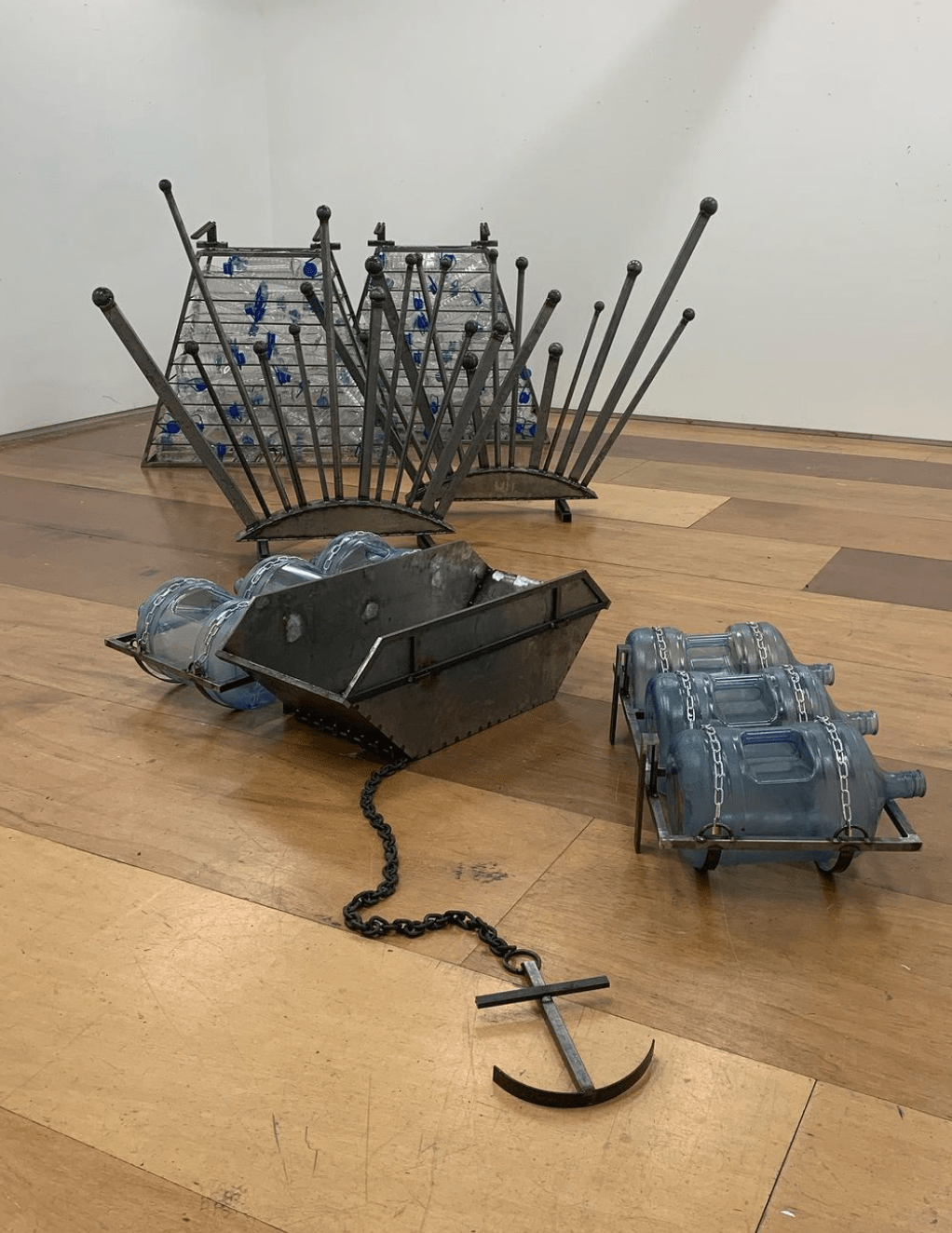 An image of several metal objects, including a skip chained to an anchor, sat on a wooden floor.