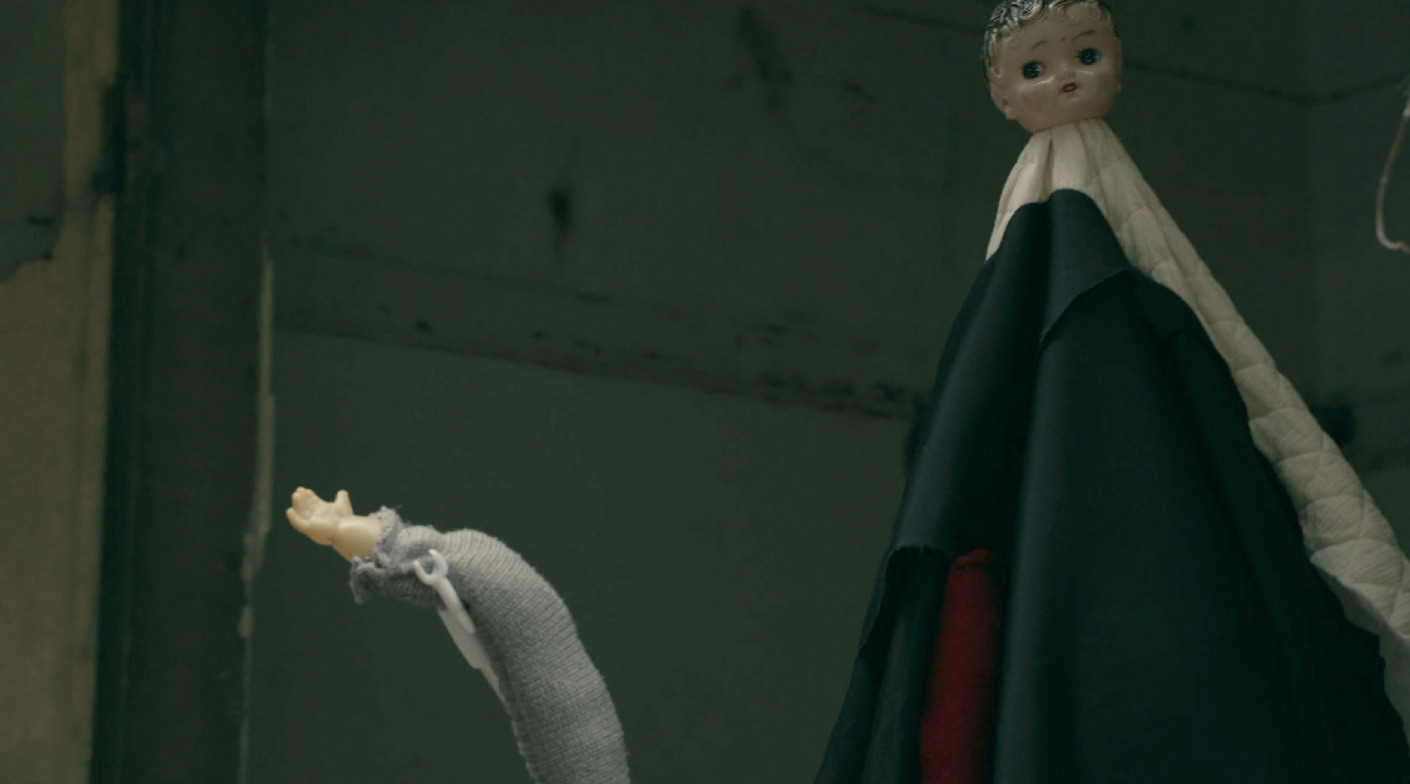 A video still of a small doll waving a long arm.