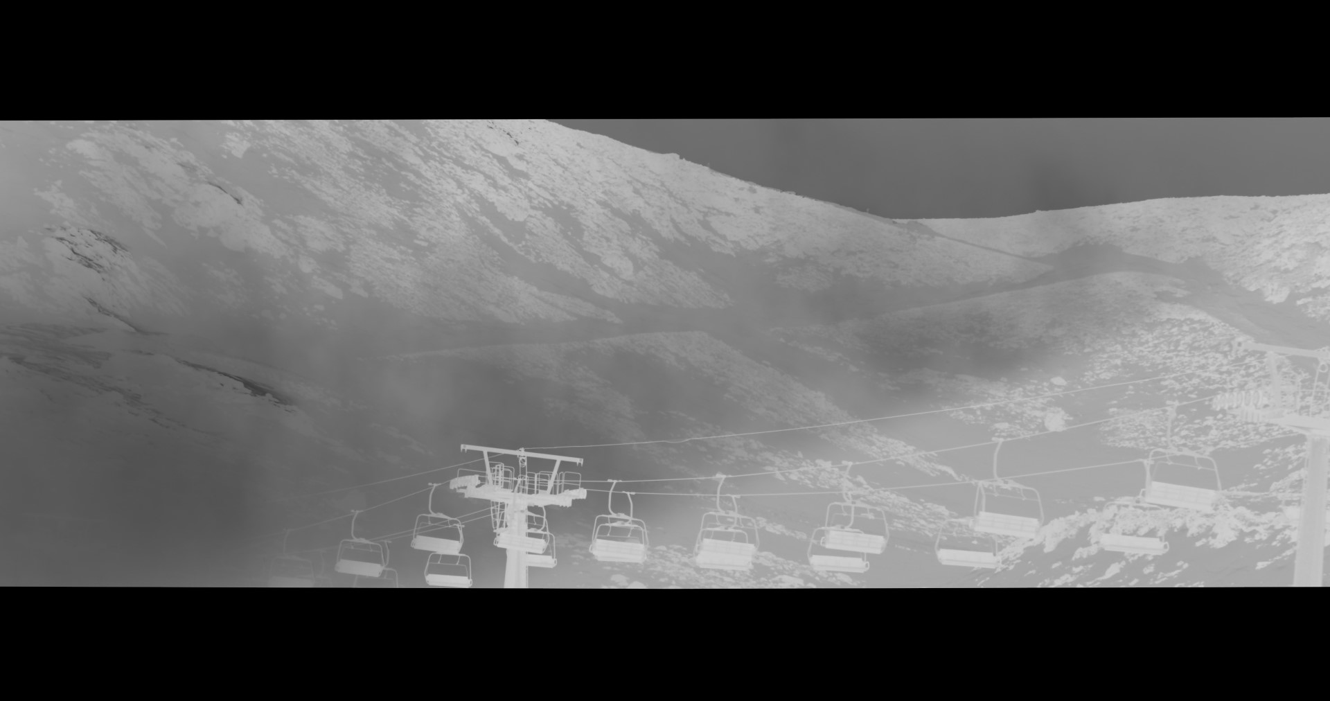 An inverted, greyscale image of a chair lift next to a mountain.