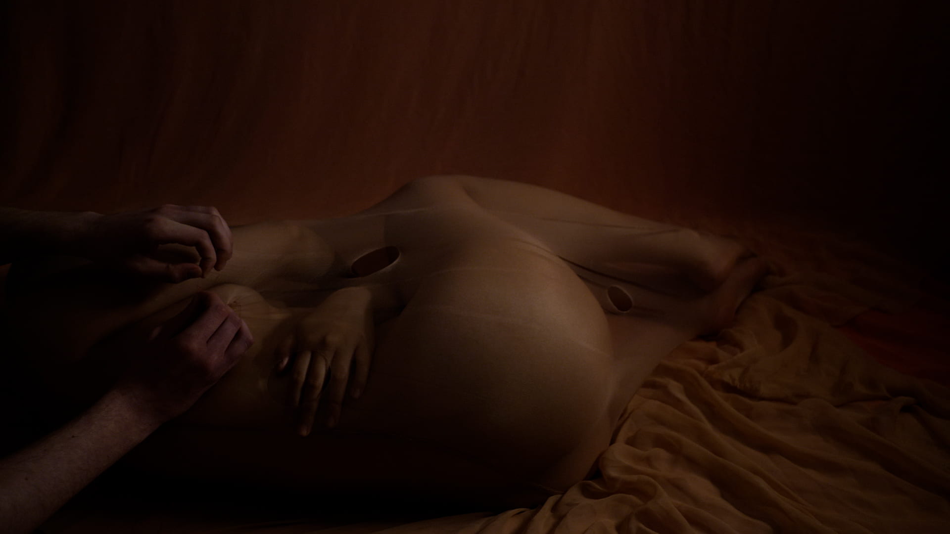 A video still of people's naked bodies in a dark space.