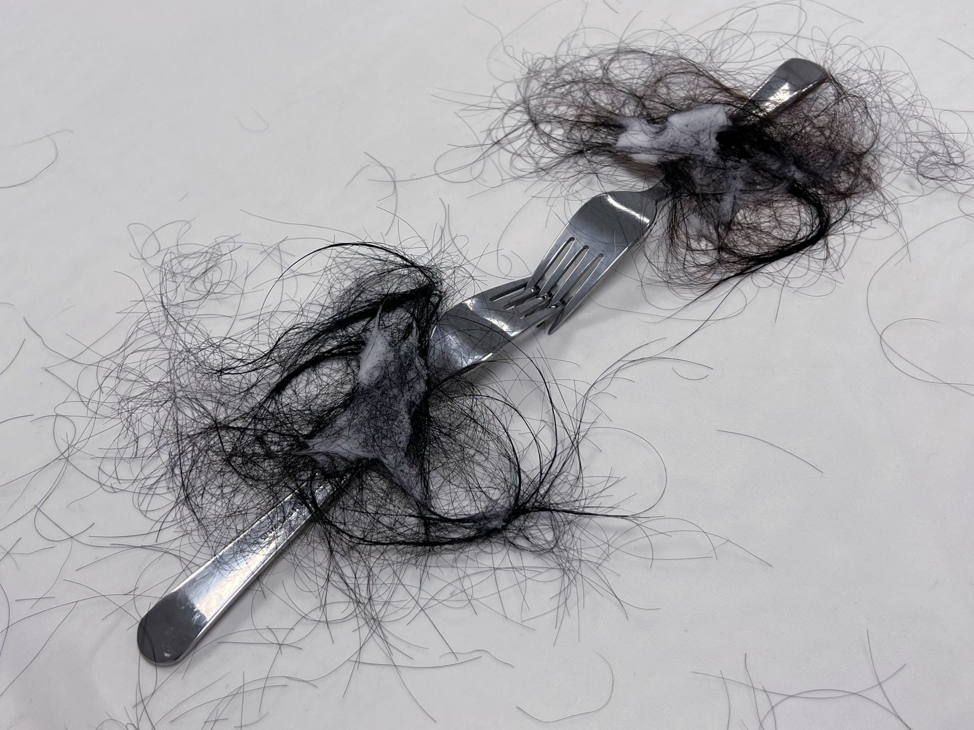 An image of forks facing each other on a table, covered in black hair.