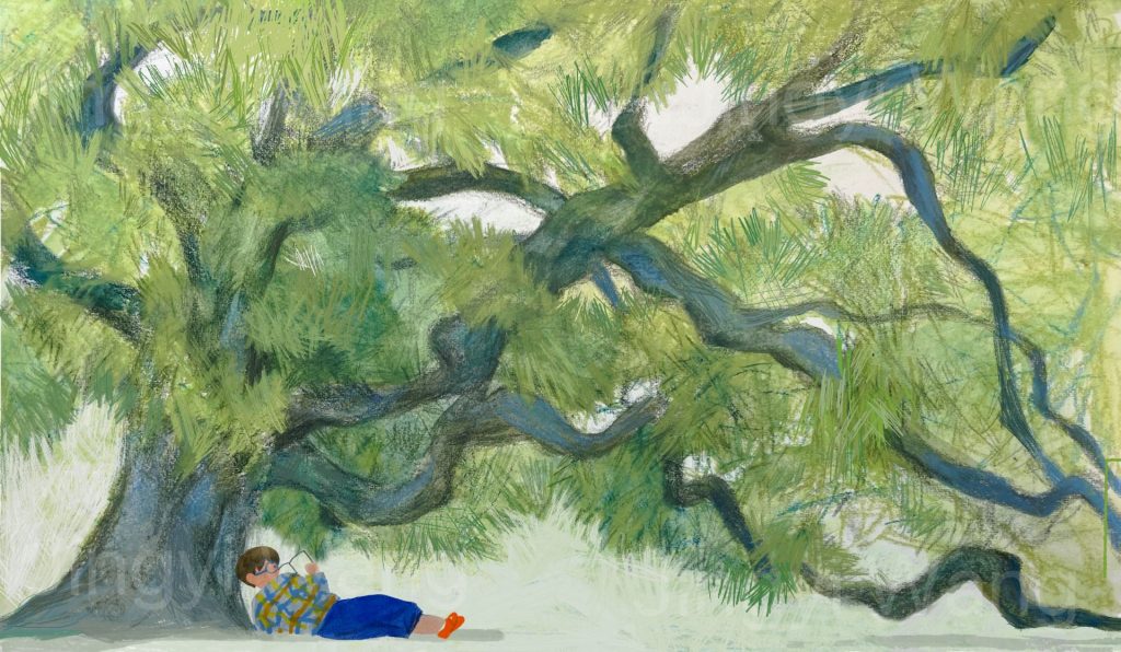 A boy is sat under a tree reading.