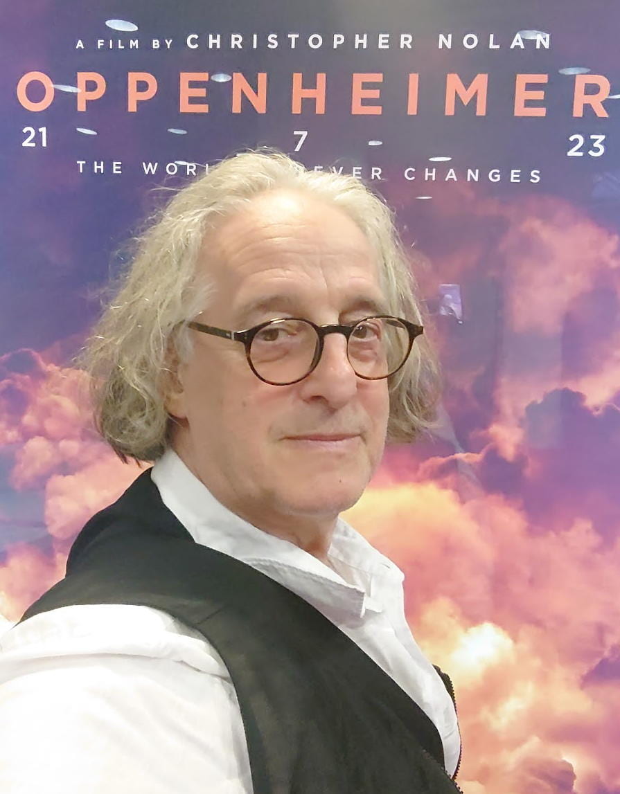 Michael Newman in front of poster of Oppenheimer