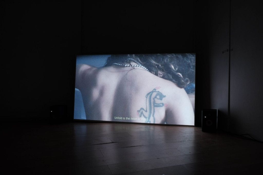 A screen showing a naked back with a tattoo across the shoulder. 