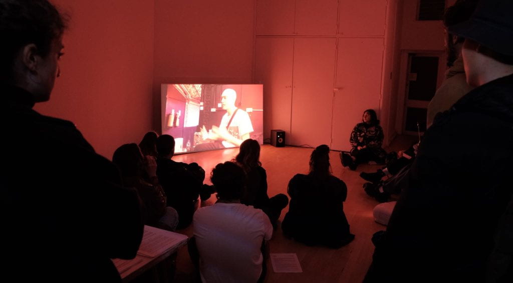 A group of people sitting watching a film in a red room. 