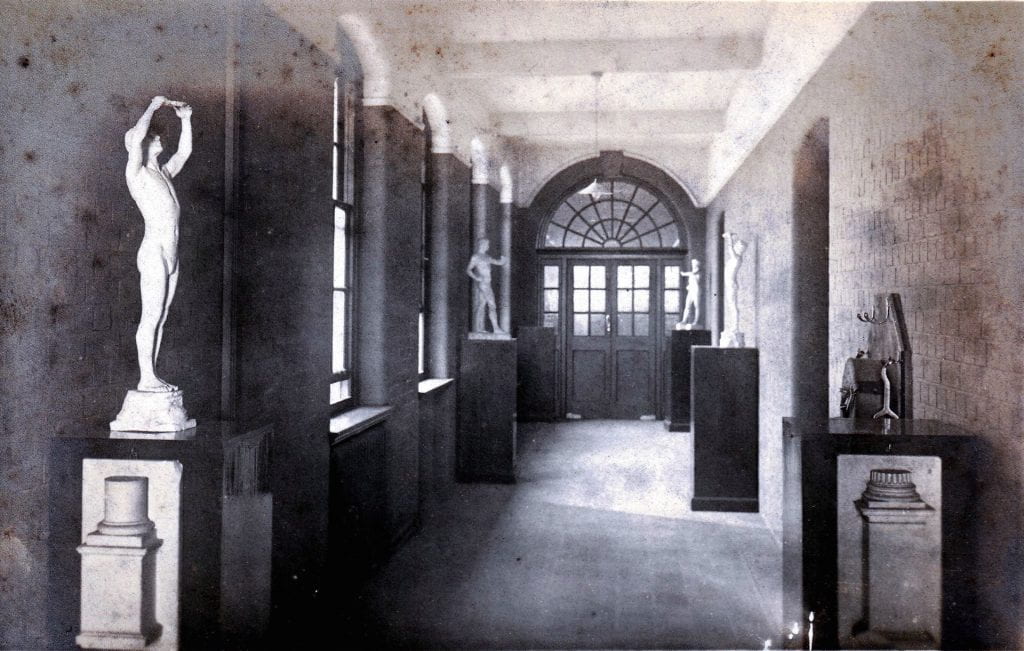 Black and white photograph of a corridor of the Blomfield building of Goldsmiths' College in 1908 with classical statues on plinths against the walls.