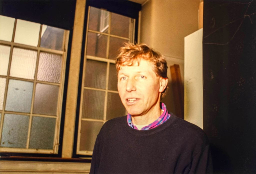 A portrait of Nigel Perkins in sweater and open necked shirt taken in studio of Goldsmiths main building in 1996.