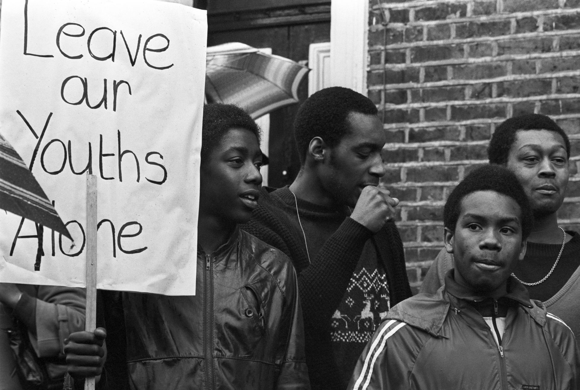 Young men standing outside with a sign that reads, 'Leave our Youths Alone'