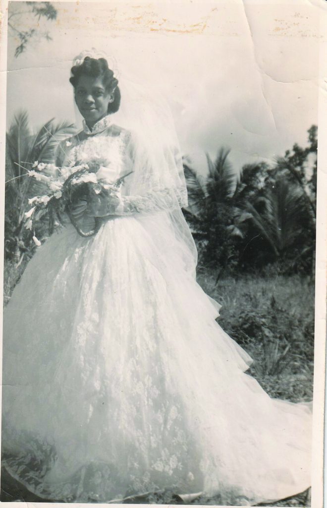 A woman stands outside in a wedding dress holding a bunch of flowers