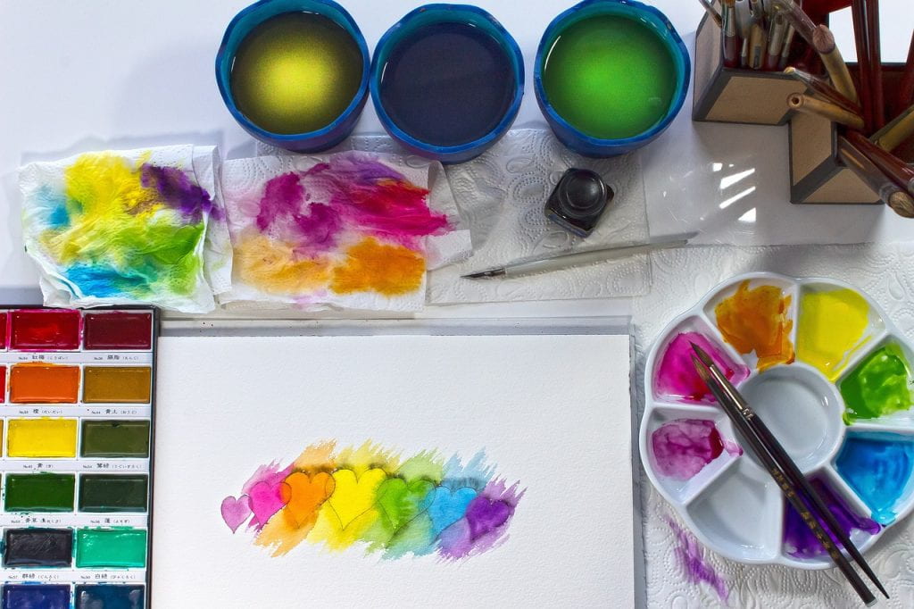 Paper with painted rainbow hearts surrounded by artists tools.