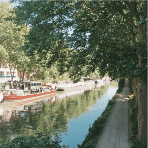 narrow river with boats parked on the left and a narrow path with overhanging trees to the right