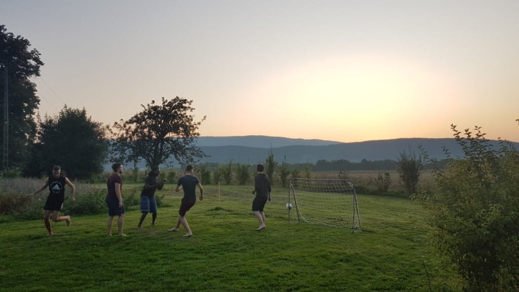people playing football outside in a green, grassy area with the sunset in the background