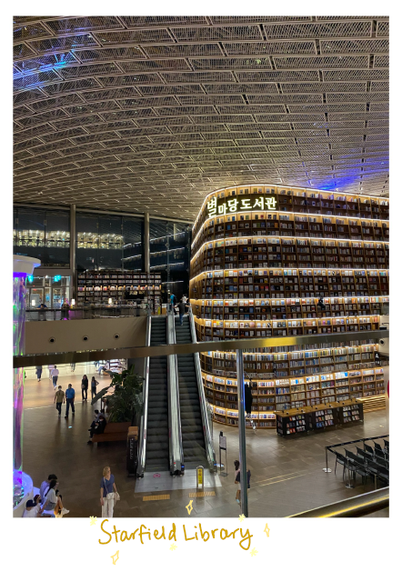 View inside a library with an escalator leading up to another flow full of shelves of books lined with fairy lights