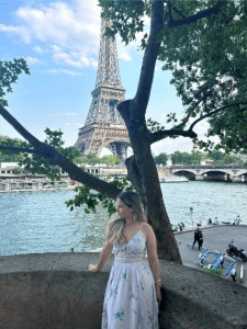young woman looking away from the camera with the base of the eiffel tower in the background on a sunny day
