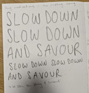 A page of a notebook is covered with hand-written script reading: "Slug Meditations - the rushing song. SLOW DOWN SLOW DOWN AND SAVOUR SLOW DOWN SLOW DOWN AND SAVOUR 'To be slow, low, shiny and curious'"